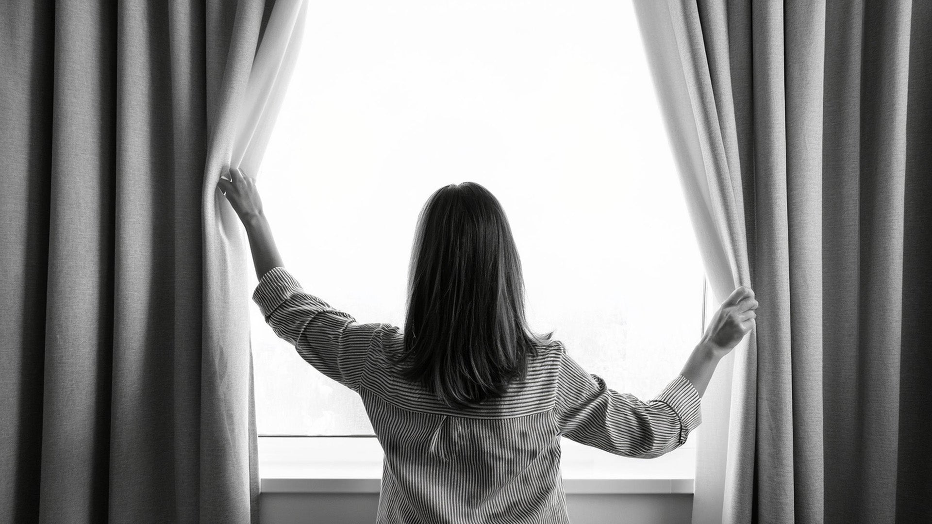 Picture of a woman opening window curtains.